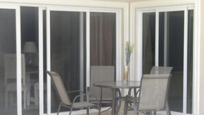 A patio area with a table and chairs, a vase with flowers, and a view through large sliding glass doors. - Villa 604 RCL (Sosúa)