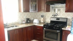 A kitchen with wooden cabinets, a stainless steel stove, a sink, and a countertop with various items. - Villa 604 RCL (Sosúa)