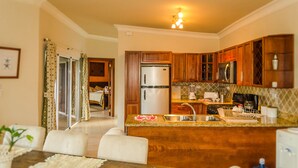 A modern kitchen with wooden cabinets, stainless steel appliances, and a dining area with a table and chairs. - Well Furnished w Private Pool, BBQ & Palapa Bar (Sosúa)