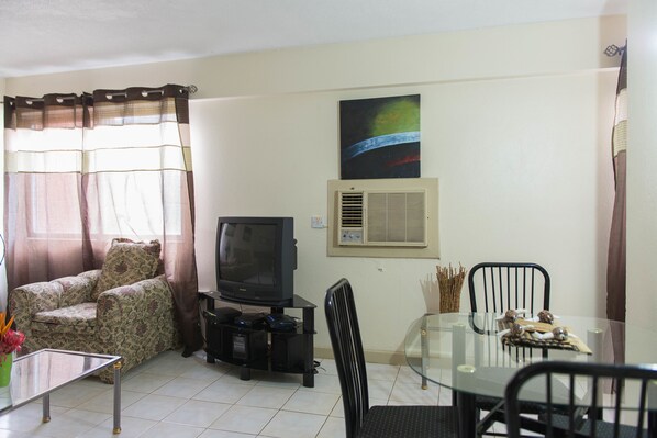 Una sala de estar con sofá, televisión, mesa de vidrio y un comedor con sillas.