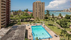 A rooftop pool with a view of the ocean and palm trees. - Turtle Towers Apartments (Ocho Rios)