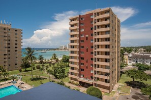 A high-rise hotel with multiple balconies, a swimming pool, and a view of the beach and ocean.