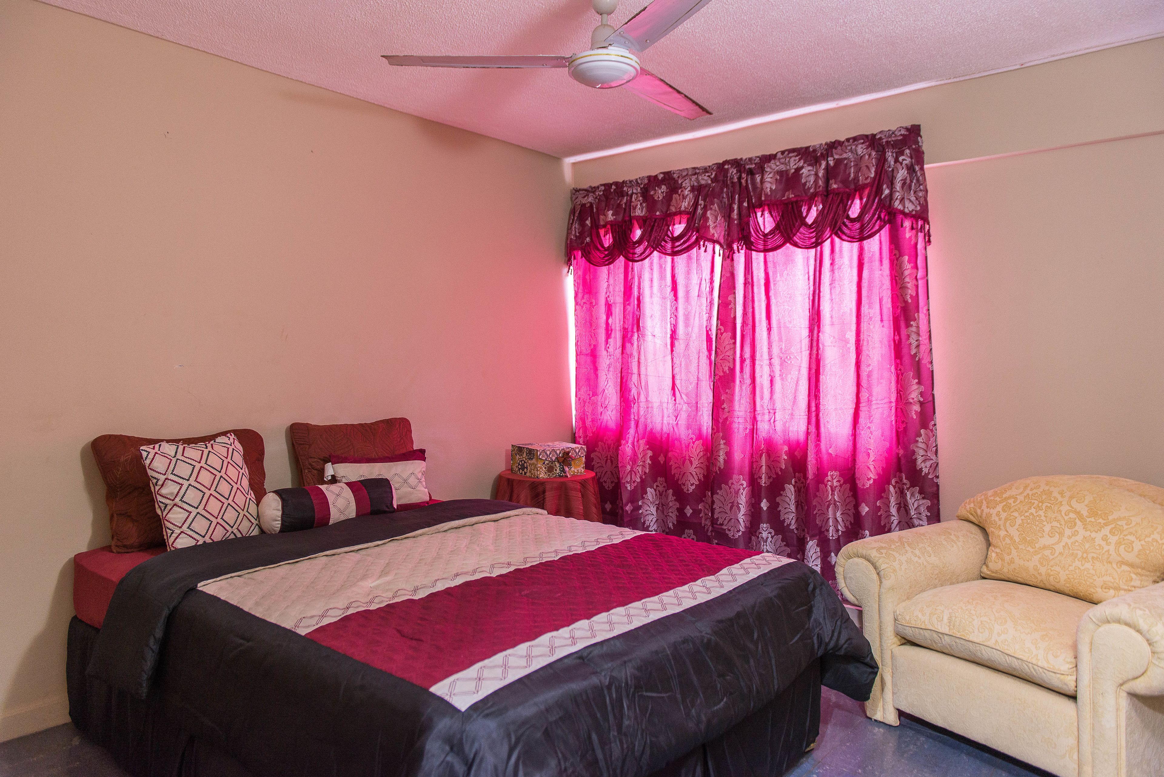 A bedroom with a bed, a chair, a ceiling fan, and curtains.