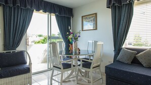 A room with a glass table surrounded by white chairs, a wicker sofa, and a dark blue couch. - Turtle Towers Apartments (Ocho Rios)