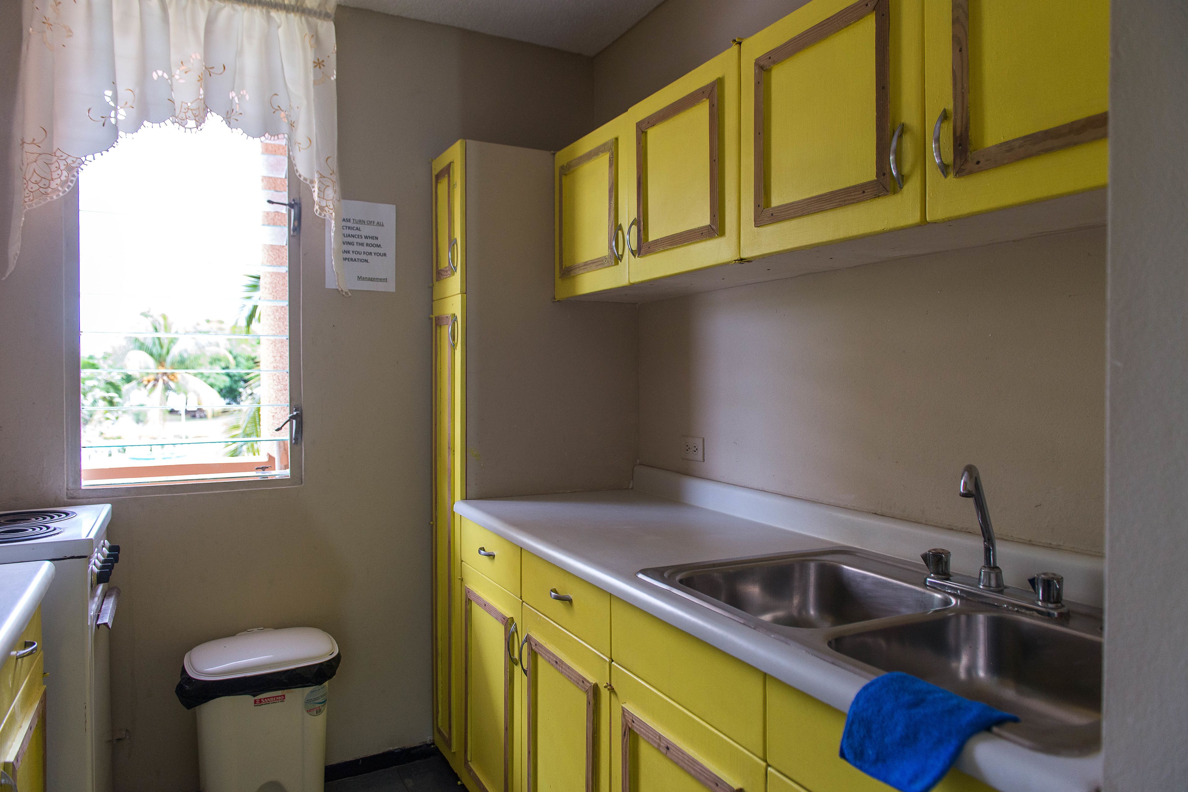 A kitchen with yellow cabinets, a stainless steel sink, and a window with a view of greenery.