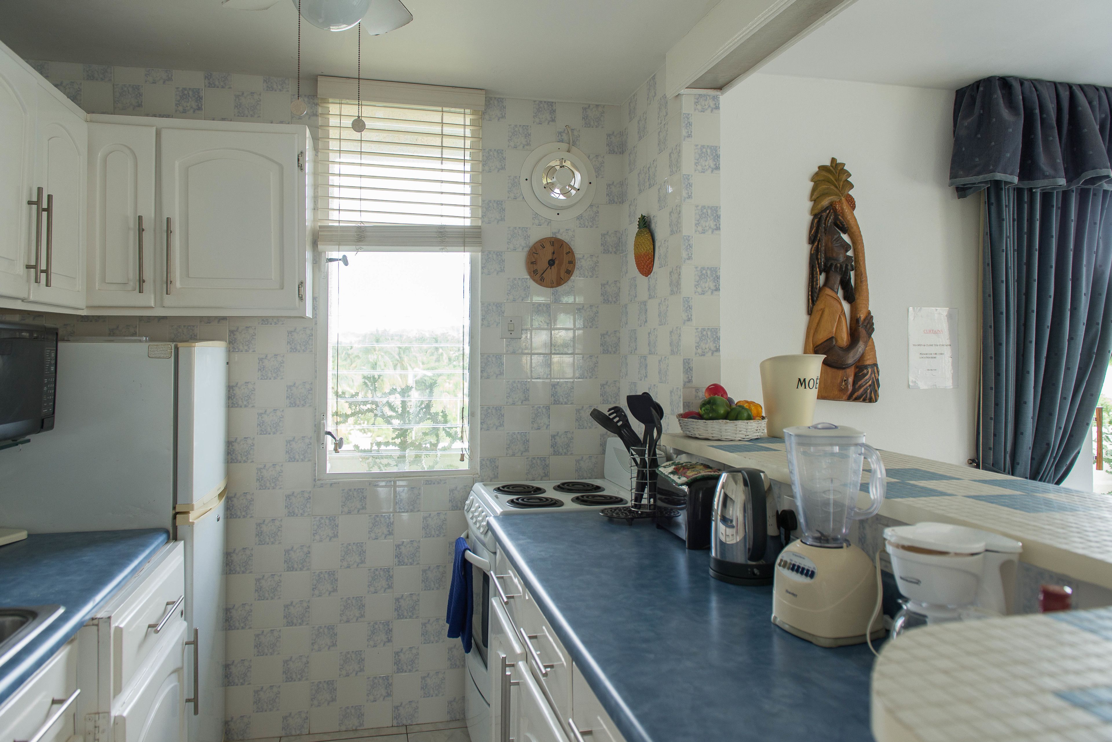 A kitchen with white cabinets, a microwave, a stove, a blender, and a window with blinds.