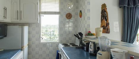 A kitchen with white cabinets, a microwave, a stove, a blender, and a window with blinds.