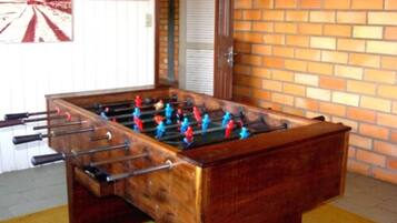 Una mesa de fútbol de madera con figuras rojas y azules, frente a una pared de ladrillo y una puerta blanca.