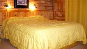 Un llit amb llençol groc en una habitació amb revestiment de fusta i parets de maó.