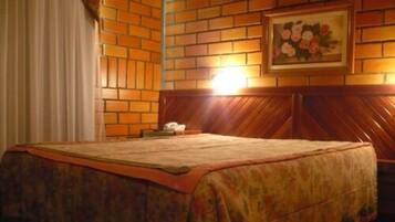 A hotel room with a brick-patterned wall, a wooden headboard, a bed with a floral bedspread, and a framed floral painting above the bed.