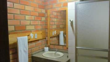 Un baño con lavamanos, espejo y toallero frente a una pared de ladrillo.