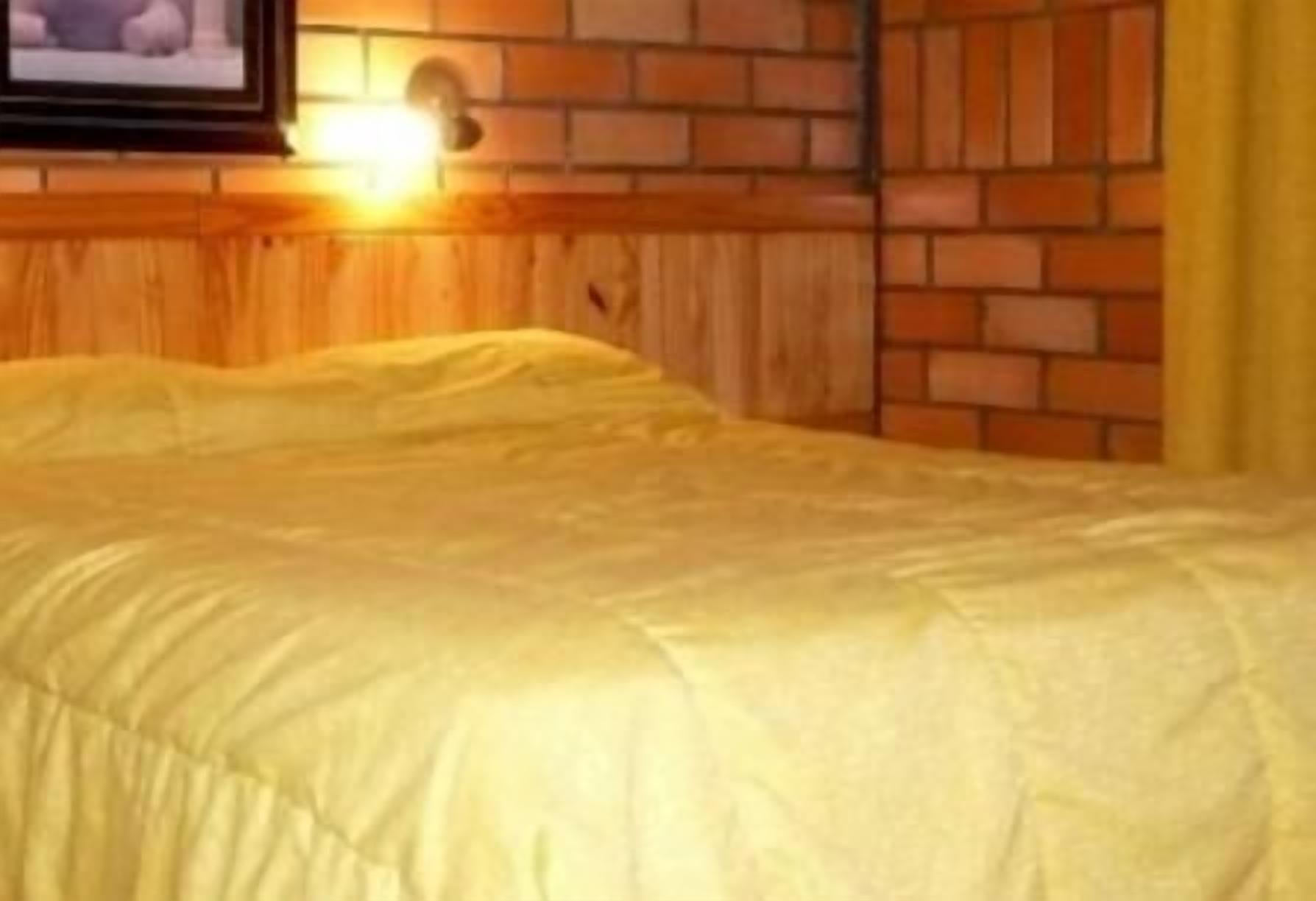 A bed with a yellow bedspread in a room with wooden paneling and a brick wall.