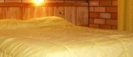Una cama con colcha amarilla en una habitación con paneles de madera y pared de ladrillo.
