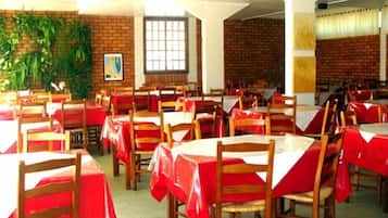 Un comedor con mesas cubiertas de manteles rojos y sillas de madera, paredes de ladrillo y un ventanal grande.