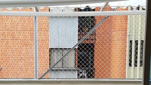 Un balcon avec deux fauteuils à bascule, un mur blanc et une vue sur un bâtiment en briques agrémenté d’une clôture en métal.