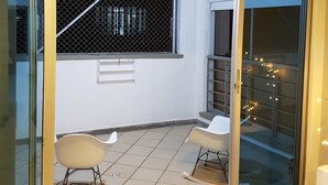 Un balcon avec deux chaises, une fenêtre ornée d’une grille métallique et un mur blanc.