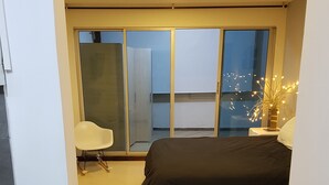 Une chambre à coucher avec un lit, une chaise, une table de chevet avec une lampe et une grande fenêtre.