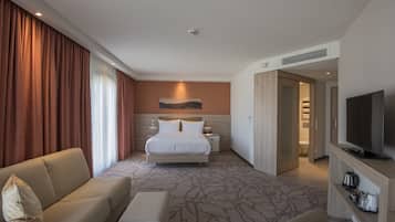 Habitación de hotel con cama, sofá, televisión y baño visible a través de una puerta abierta.