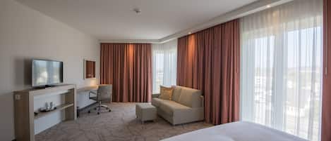 A hotel room with a large bed, a sofa, a TV, a desk, and a chair.