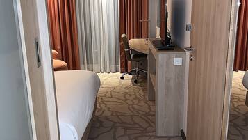 A hotel room with a bed, a desk with a chair, a television, and a window with curtains.