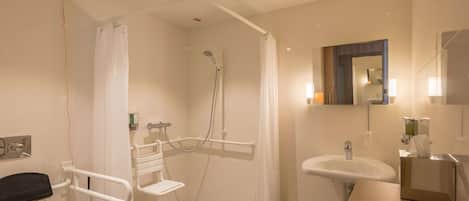 A modern bathroom with a shower, toilet, and sink, equipped with a handrail and grab bars for accessibility.