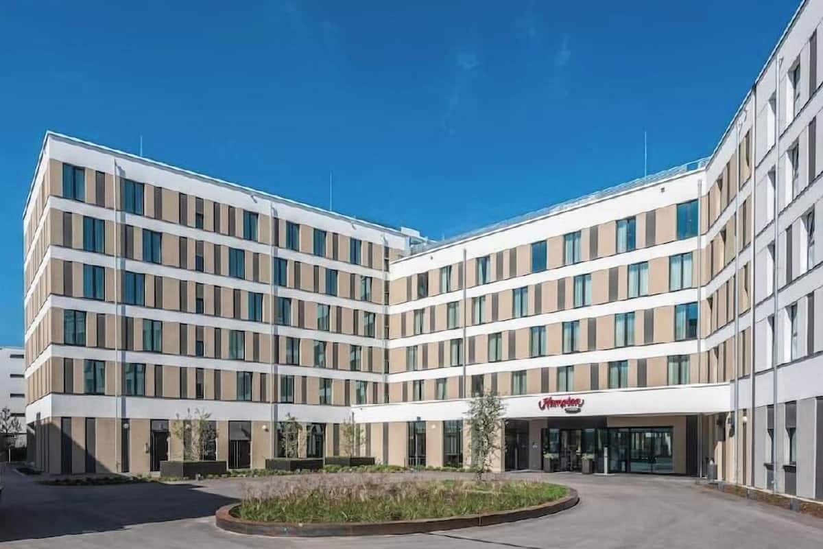 Un hôtel moderne à plusieurs étages, doté d’un toit plat, de grandes fenêtres et d’une entrée centrale.