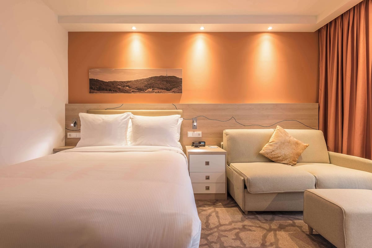 Une chambre d’hôtel moderne, dotée d’un grand lit, d’un canapé, d’une table de chevet et d’une œuvre d’art accrochée au mur.