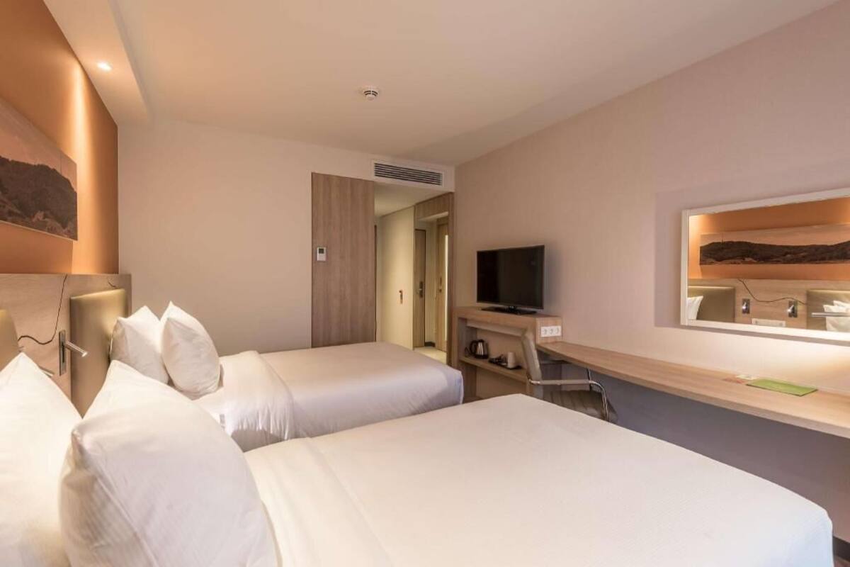 Une chambre d’hôtel avec deux lits, une télévision, un bureau avec un miroir et un tableau au mur.