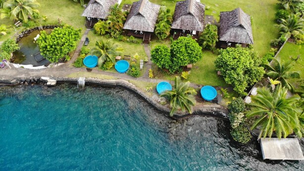 Un resort con varias cabañas de techo de paja, piscina y exuberante vegetación tropical.