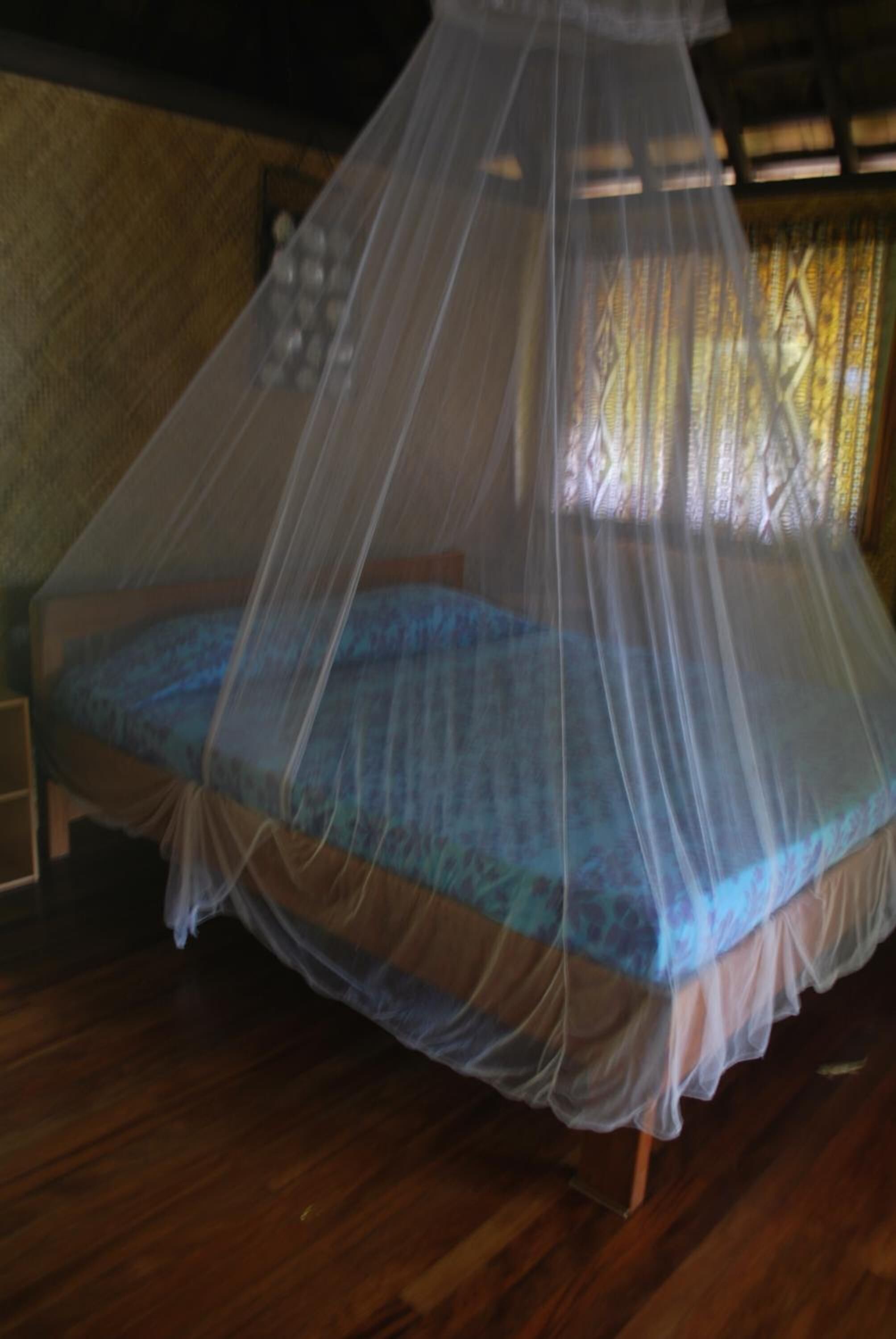 A bed with a mosquito net, wooden floor, and a patterned wall.