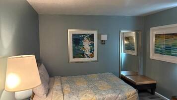 A hotel room with a bed, a bedside lamp, a chair, and two framed artworks on the wall.