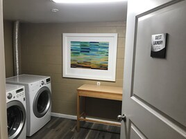 Un área de lavandería con dos lavadoras, un banco de madera y un cuadro abstracto enmarcado en la pared.