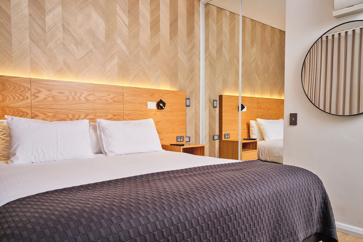 Une chambre d’hôtel moderne avec un grand lit, une tête de lit en bois et un miroir.