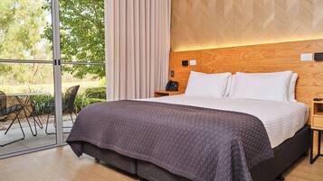 A modern hotel room with a large bed, a wooden headboard, a glass door leading to an outdoor area, and a small table with a phone.