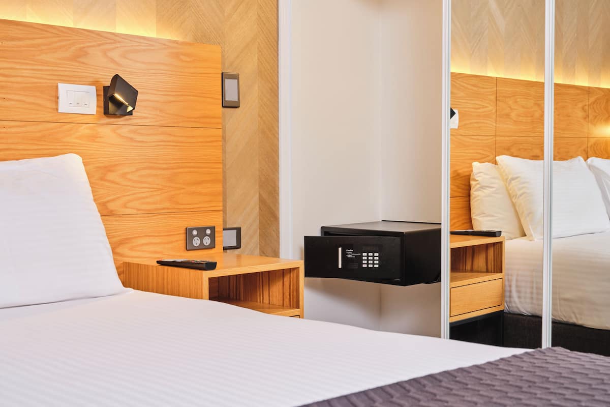 Une chambre d’hôtel équipée d’un lit, d’une tête de lit en bois, de tables de chevet, d’un mini-bar et d’un panneau de commande.
