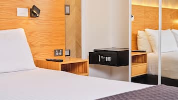 A hotel room with a bed, wooden headboard, bedside tables, a minibar, and a control panel.