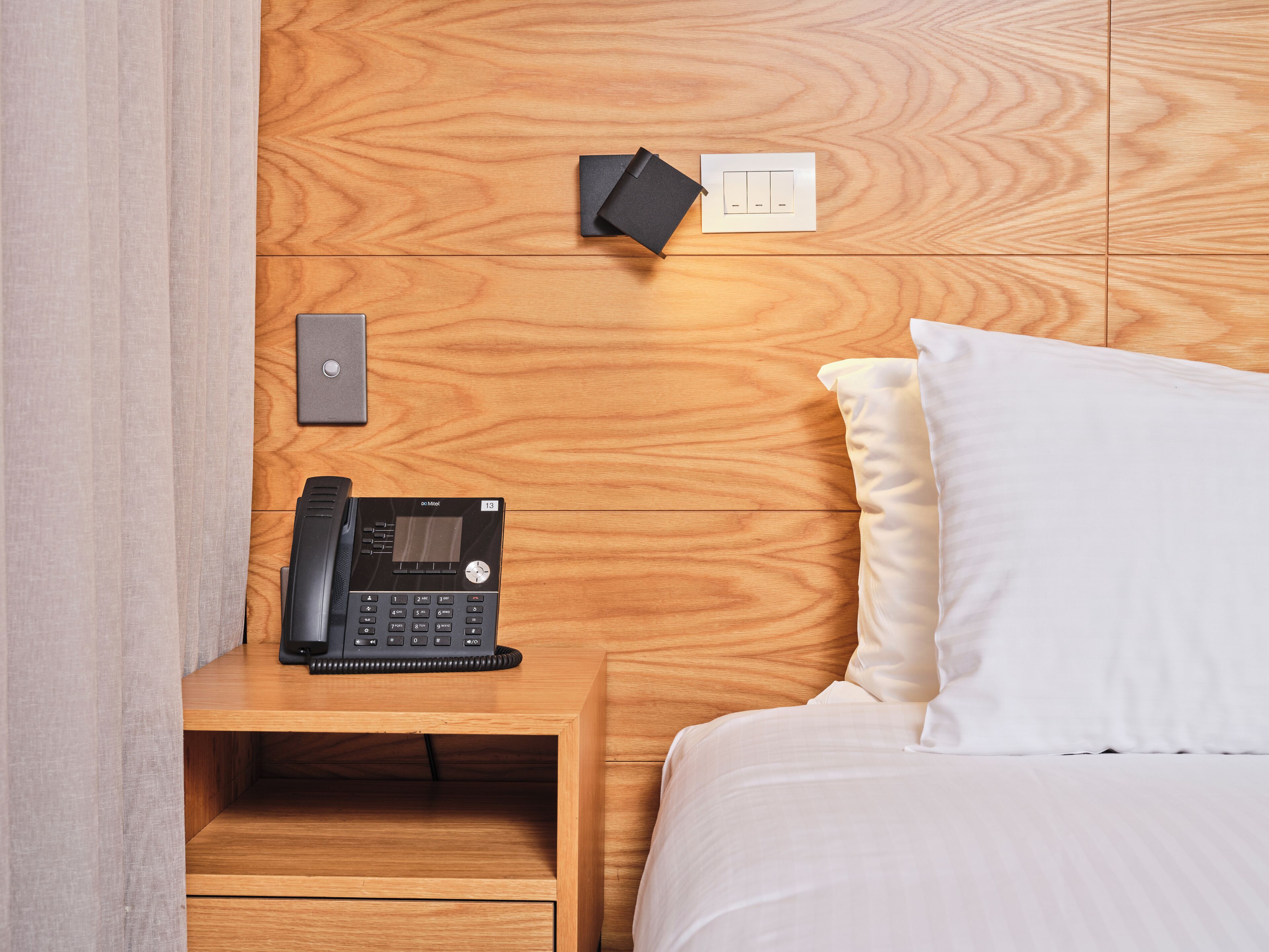 Ein hölzerner Kopfseitenverkleiderung mit integriertem Telefon und Steckdose, eine Nachttischschublade und ein weißes Kissen auf einem Bett.