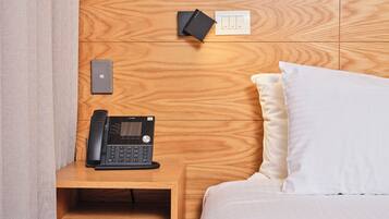 Ein hölzerner Kopfseitenverkleiderung mit integriertem Telefon und Steckdose, eine Nachttischschublade und ein weißes Kissen auf einem Bett.
