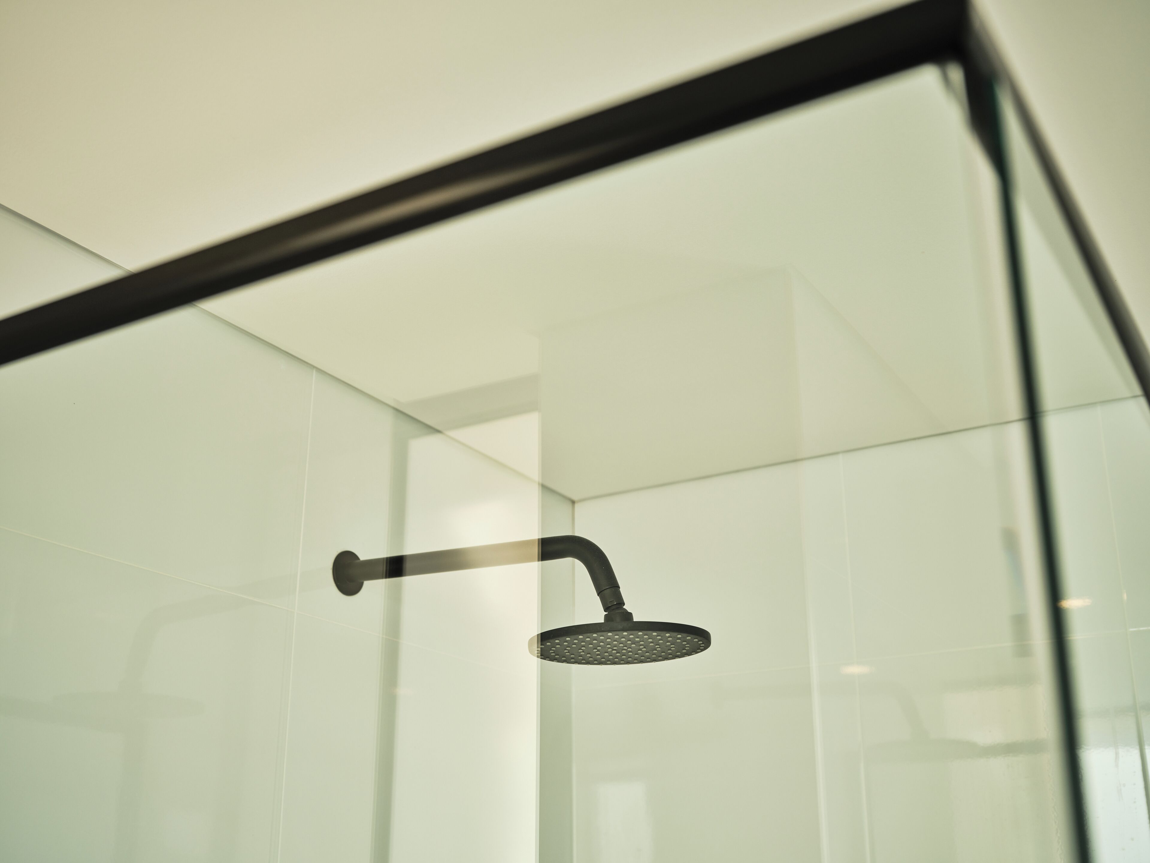 A modern shower enclosure with a glass door and a black showerhead.