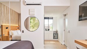 Quarto de hotel moderno com cama, espelho redondo, pequeno kitchenette e televisão.