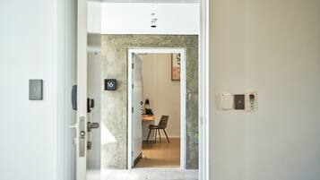 A hallway leading to a room with a desk, chair, and a phone. A number '16' is visible on the wall.