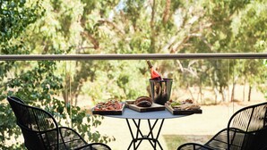 Uma varanda com uma mesa posta para refeição, rodeada por cadeiras e com vista para um jardim exuberante.