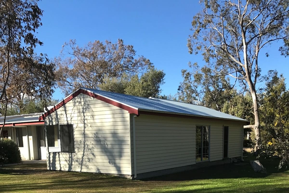 Een gelijkvloers huis met een rood dak en beige gevelbekleding, omgeven door een verzorgd gazon en bomen.