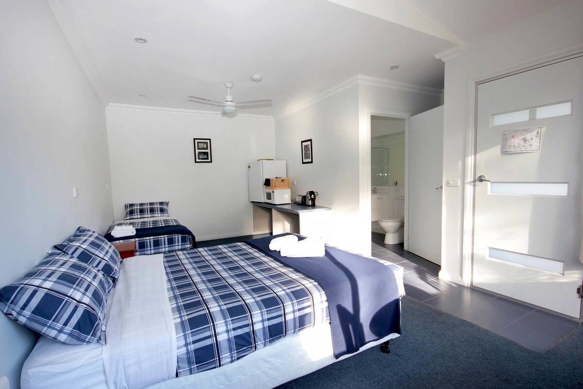 Een slaapkamer met twee bedden, een plafondventilator, een magnetron en een kleine kitchenette.