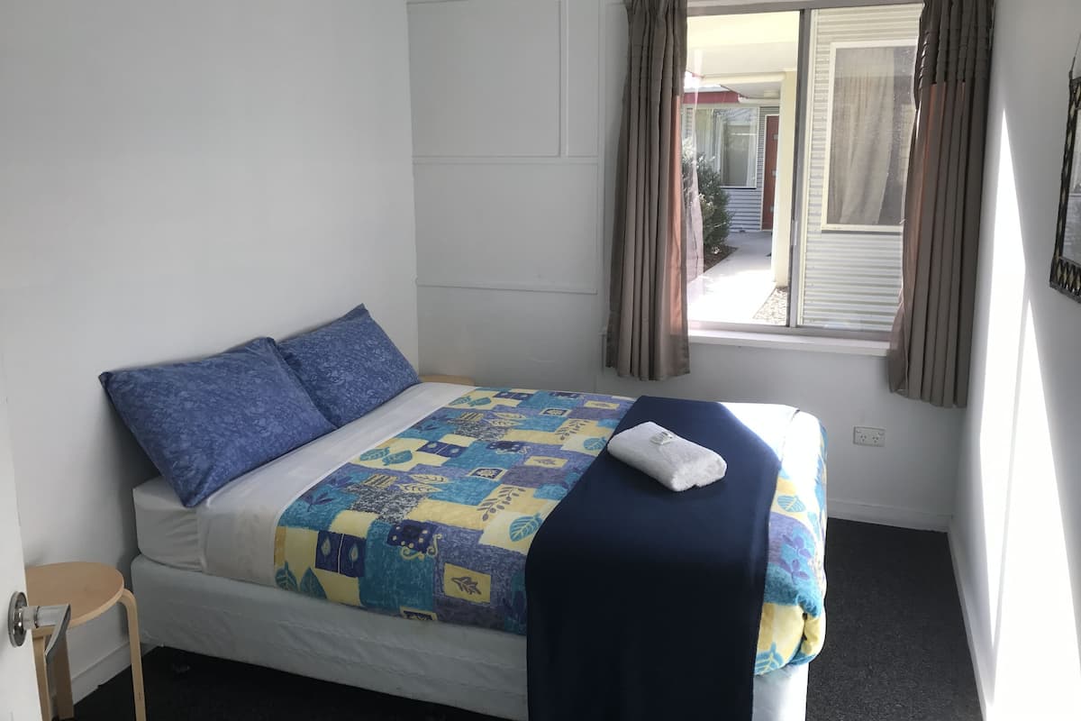 Een eenpersoonsbed met een deken in blauw en geel, een witte matras en twee blauwe kussens.