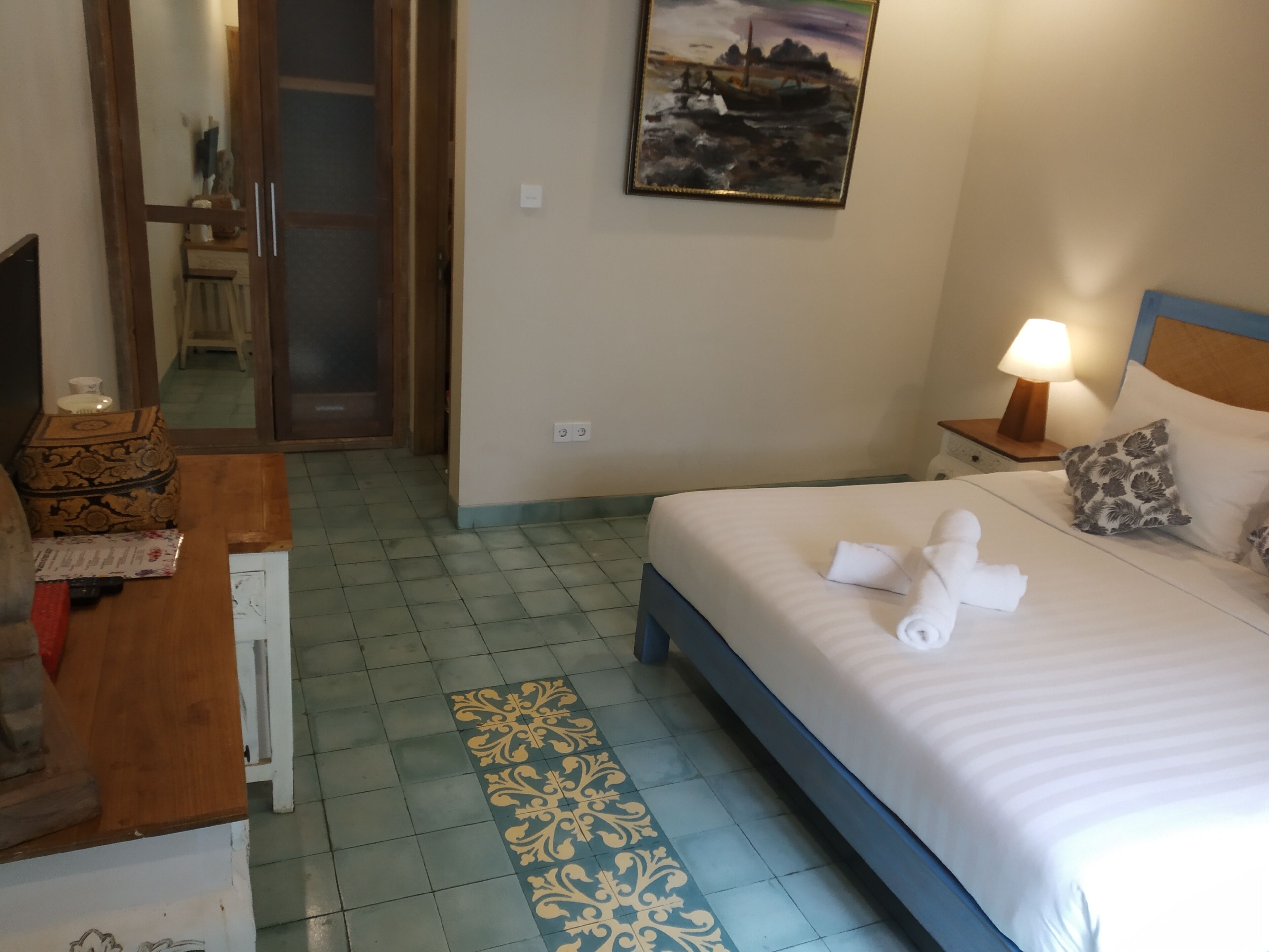 A hotel room with a bed, a desk, a lamp, and a painting on the wall.