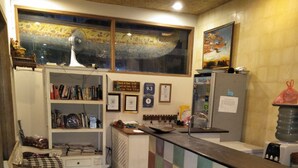 A small, cozy kitchen with a check-in counter, a bookshelf, and a refrigerator. - Jukung Guest House (Denpasar)