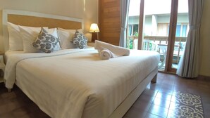 A hotel room with a large bed, a wooden headboard, a nightstand with a lamp, and a view of the outdoors through a sliding door. - Jukung Guest House (Denpasar)