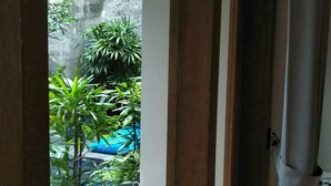 A view from a room with a wooden door leading to a balcony. The balcony has a checkered floor and a wooden chair. - Jukung Guest House (Denpasar)