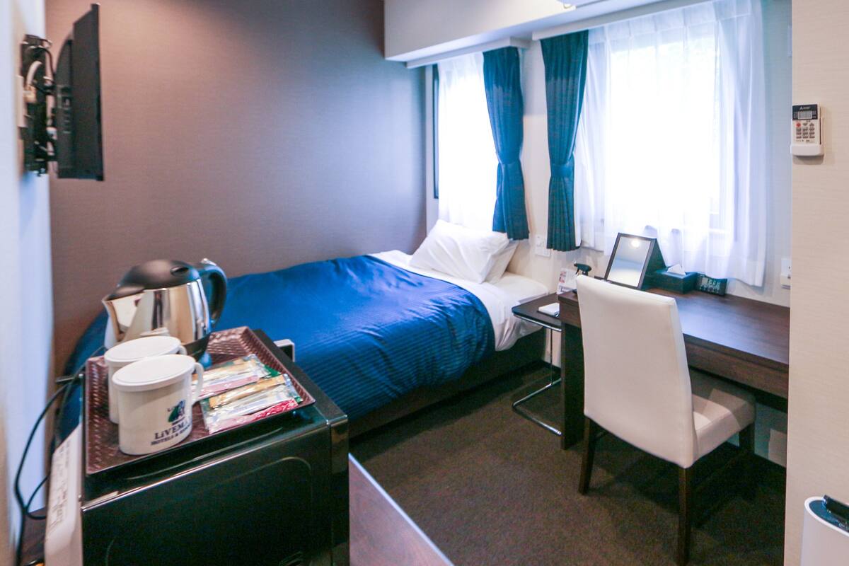 A hotel room with a bed, a desk, a chair, a coffee machine, and a window with curtains.